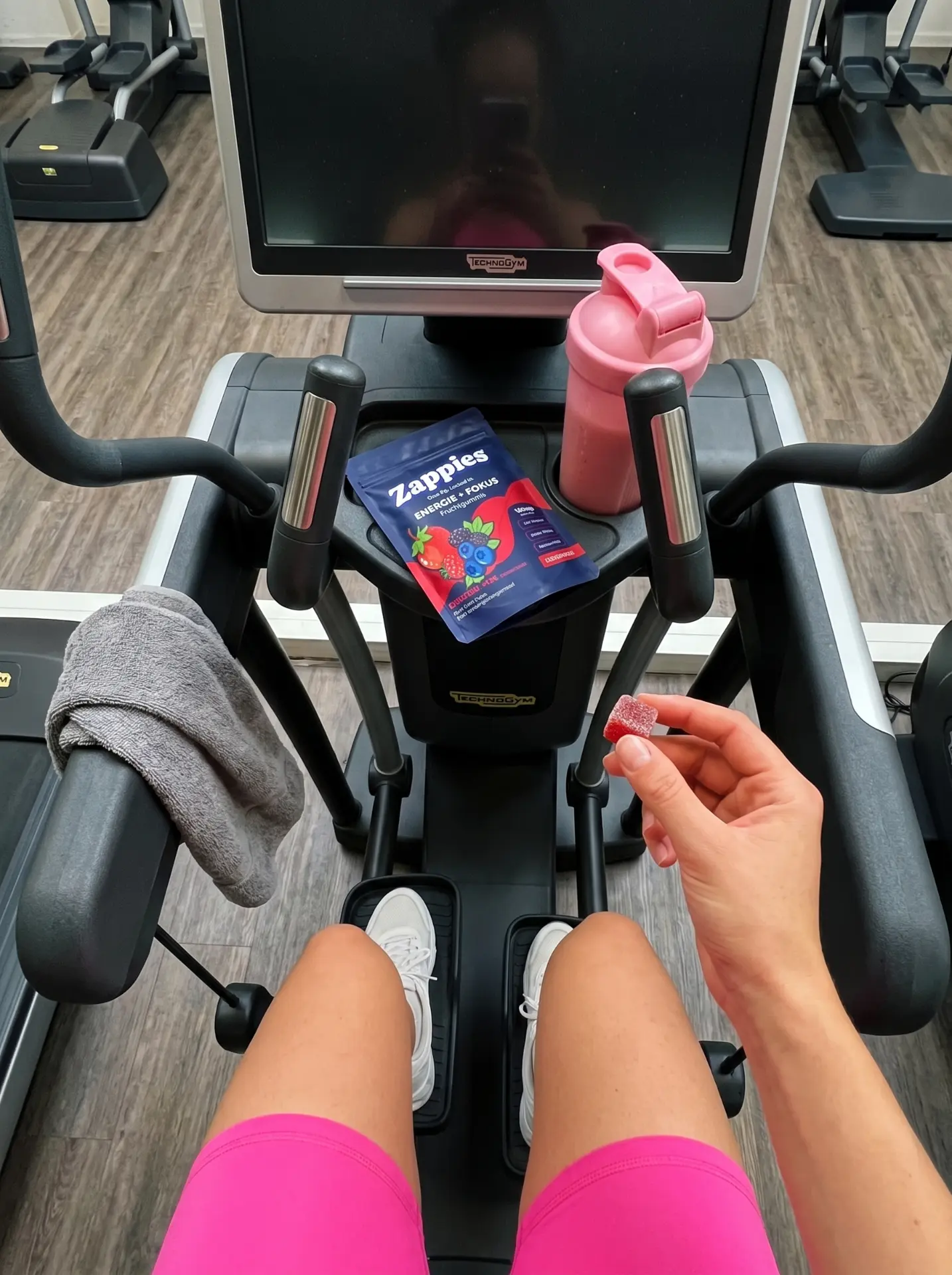 Hand hält einen ZAPPIES Fruchtgummi im Fitnessstudio vor dem Cardio-Gerät