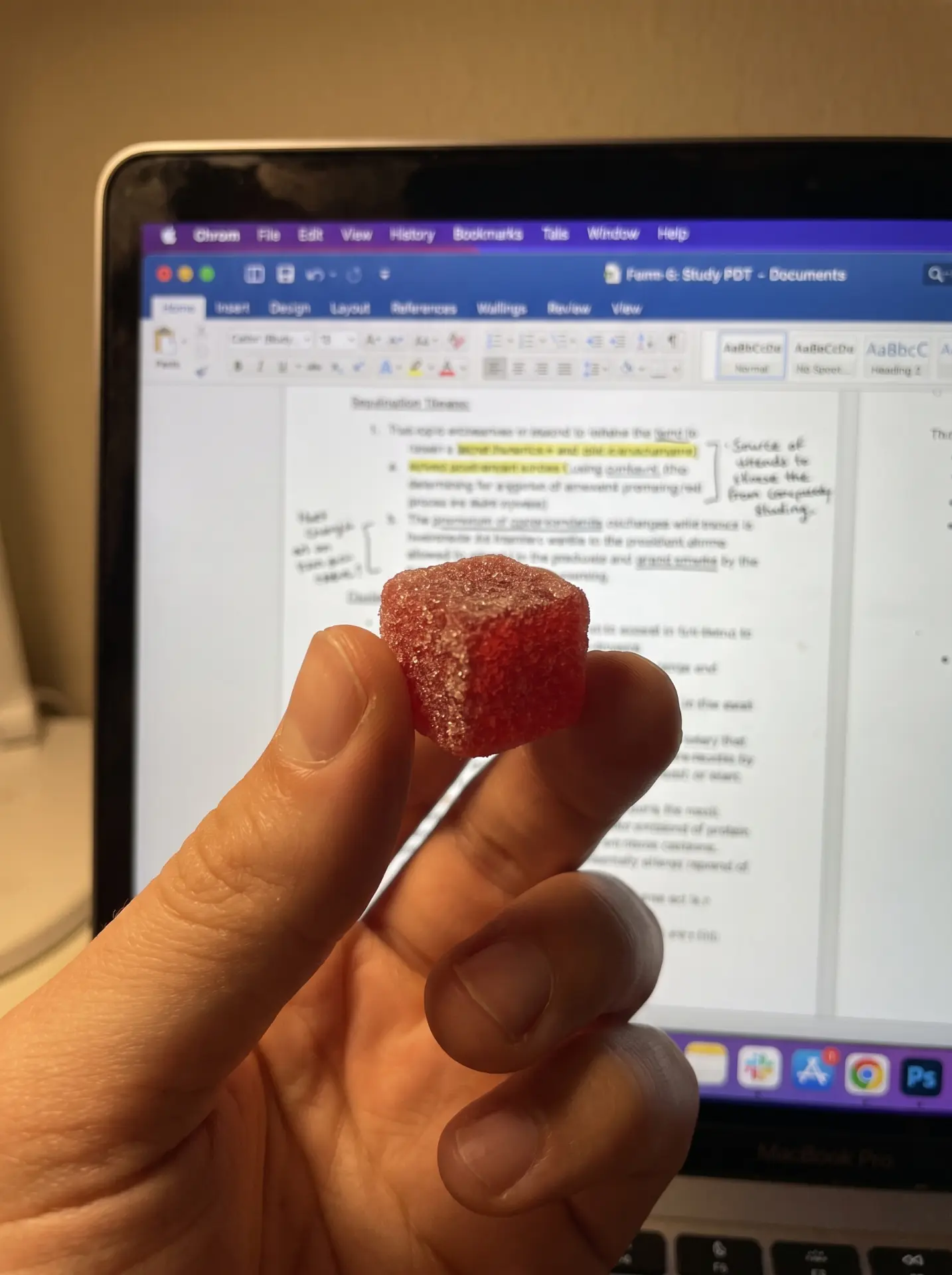 Hand hält ein ZAPPIES Fruchtgummi vor einem Laptop mit Lernunterlagen